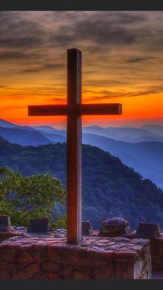 a cross on top of a mountain with the sun setting in the distance behind it