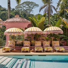 lounge chairs and umbrellas by the side of a swimming pool with palm trees in the background