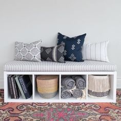 a white bench with several pillows and blankets on it next to a rug in front of a wall