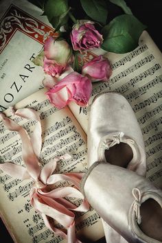 pink roses and ballet shoes sitting on top of an old music book with sheet music