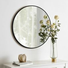 a mirror on the wall above a white table with flowers in it and a gold vase