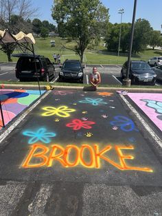 a woman is sitting on the sidewalk in front of a parking lot that has been painted with bright colors