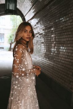 a woman in a white dress standing next to a brick wall with stars on it