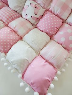 pink and white pillows with pompom trims on the edges are arranged in a heart shape