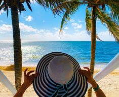 a person sitting on a beach with a hat over their head looking out at the ocean