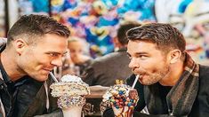 two men sitting next to each other drinking milkshakes