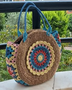 a crocheted bag sitting on top of a table next to a railing with trees in the background