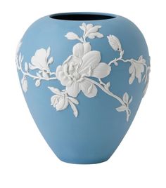 a blue vase with white flowers and leaves on it's sides, against a white background