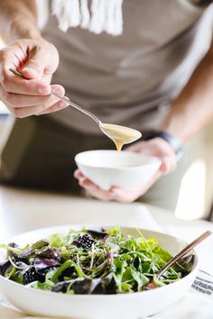 a person holding a spoon over a bowl filled with greens and blackberries on top of a table