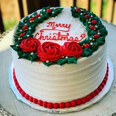 a christmas cake decorated with holly wreaths and red roses on top is sitting on a table