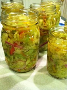 several jars filled with pickled vegetables on top of a white tablecloth covered table