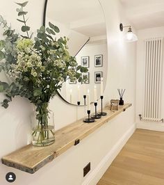 a vase filled with flowers sitting on top of a wooden shelf next to a mirror