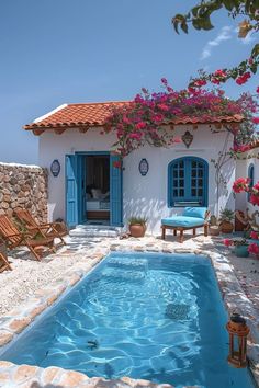 an outdoor swimming pool in front of a white house with blue shutters and doors