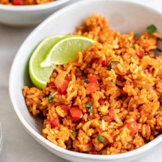 two white bowls filled with rice and garnished with cilantro, lime wedges