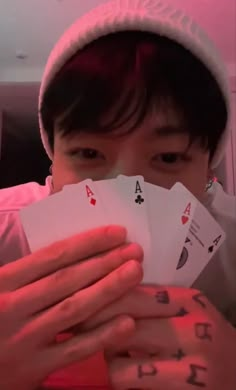 a person holding four playing cards in their hands while wearing a white hat and pink shirt