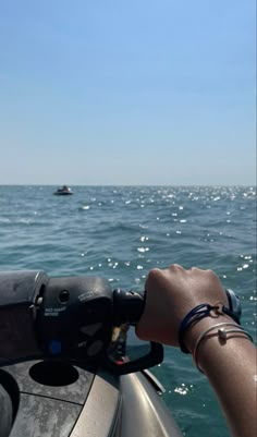 a hand on the steering wheel of a motorboat in the ocean with another boat in the distance