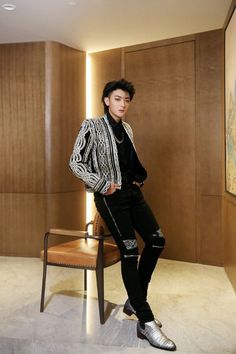 a young man sitting on top of a wooden chair next to a wall with paintings