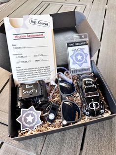 an open box with several items in it on a wooden flooring surface, including sunglasses and keys