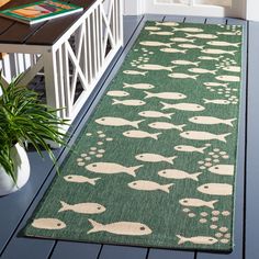 a green rug with fish on it next to a white door and potted plant