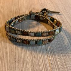 This hand stitched wrap bracelet is made with tile bead in shades of sage, cream, and caramel. Stitched onto supple 1.5 metallic bronze leather cord and finished with bronze button. Wraps around twice. Adjustable. 6 - 7 inches Jewellery Bracelets, Beaded Bracelets, Leather Cord, Hand Stitched, Wrap Around, Hand Stitching, Wrap Bracelet, Leather Bracelet, Jewelry Bracelets