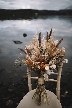 a white chair with flowers and feathers on it sitting in front of a body of water