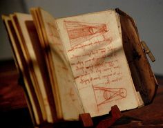 an open book with drawings on it sitting on top of a wooden table next to a pen