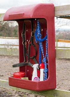 a red box with blue rope and other items in it sitting on the side of a wooden fence