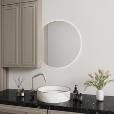 a white sink sitting under a round mirror on top of a black counter next to wooden cabinets