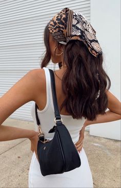 a woman with her back to the camera wearing a white tank top and black purse