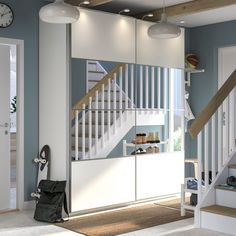 a living room with white furniture and stairs in the background is a staircase leading up to a second floor