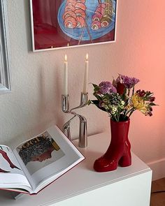 a red vase filled with flowers sitting on top of a table next to a book