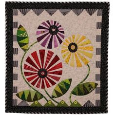 a quilted wall hanging with colorful flowers and leaves on the front, along with black border