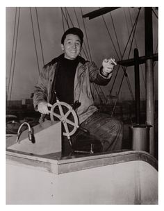 a man sitting on top of a boat holding a steering wheel in his right hand