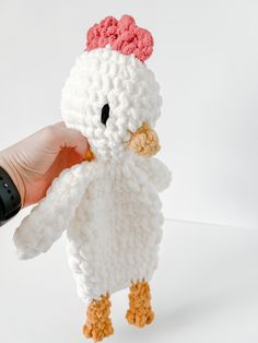 a crocheted chicken is being held up by a person's hand on a white background