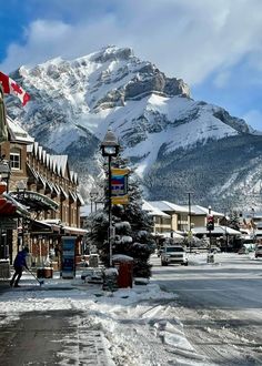 a town with mountains in the background and snow on the ground, people are walking down the street