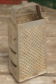 an old metal grater sitting on top of a wooden table with holes in it