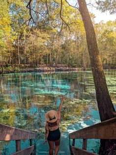 a woman in a hat is walking down the stairs to a lake with clear blue water