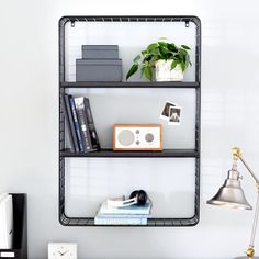 a black shelf with books and other items on it next to a lamp, clock and desk