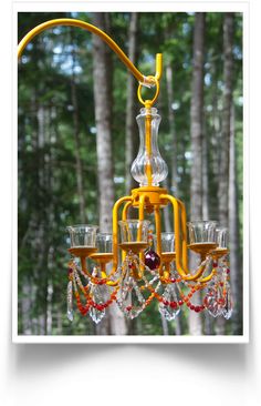 a yellow chandelier hanging from the ceiling in front of trees with crystal wine glasses on it