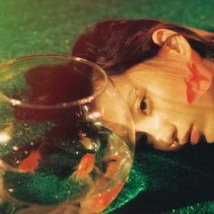 a doll laying on the ground next to a glass bowl with goldfish in it