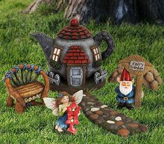 gnomes and fairy figurines are sitting in the grass near a teapot