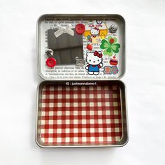 an open tin with a hello kitty design on the lid and red checkered table cloth