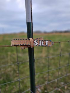 a wooden ski sign attached to a fence post in front of a green field with grass