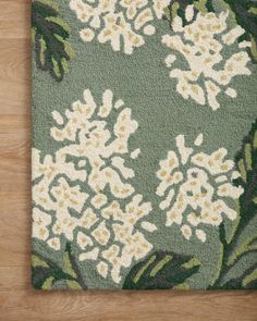 a green rug with white flowers and leaves on top of wooden flooring next to a wall