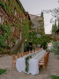 an outdoor dining table set up with white linens and greenery on the wall