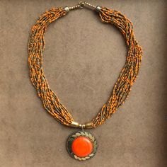 an orange beaded necklace with a pendant hanging from it's center, on a brown surface