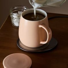 a cup of coffee is being poured into it with a saucer next to it