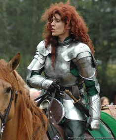 a woman dressed as a knight riding on the back of a brown horse with red hair