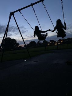 two children are playing on swings at dusk