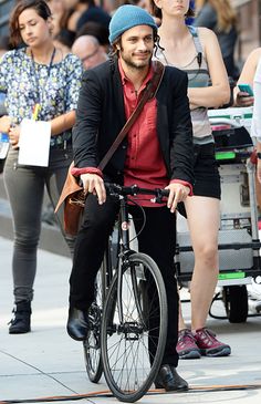 a man riding a bike down the street with other people walking around him and onlookers behind him